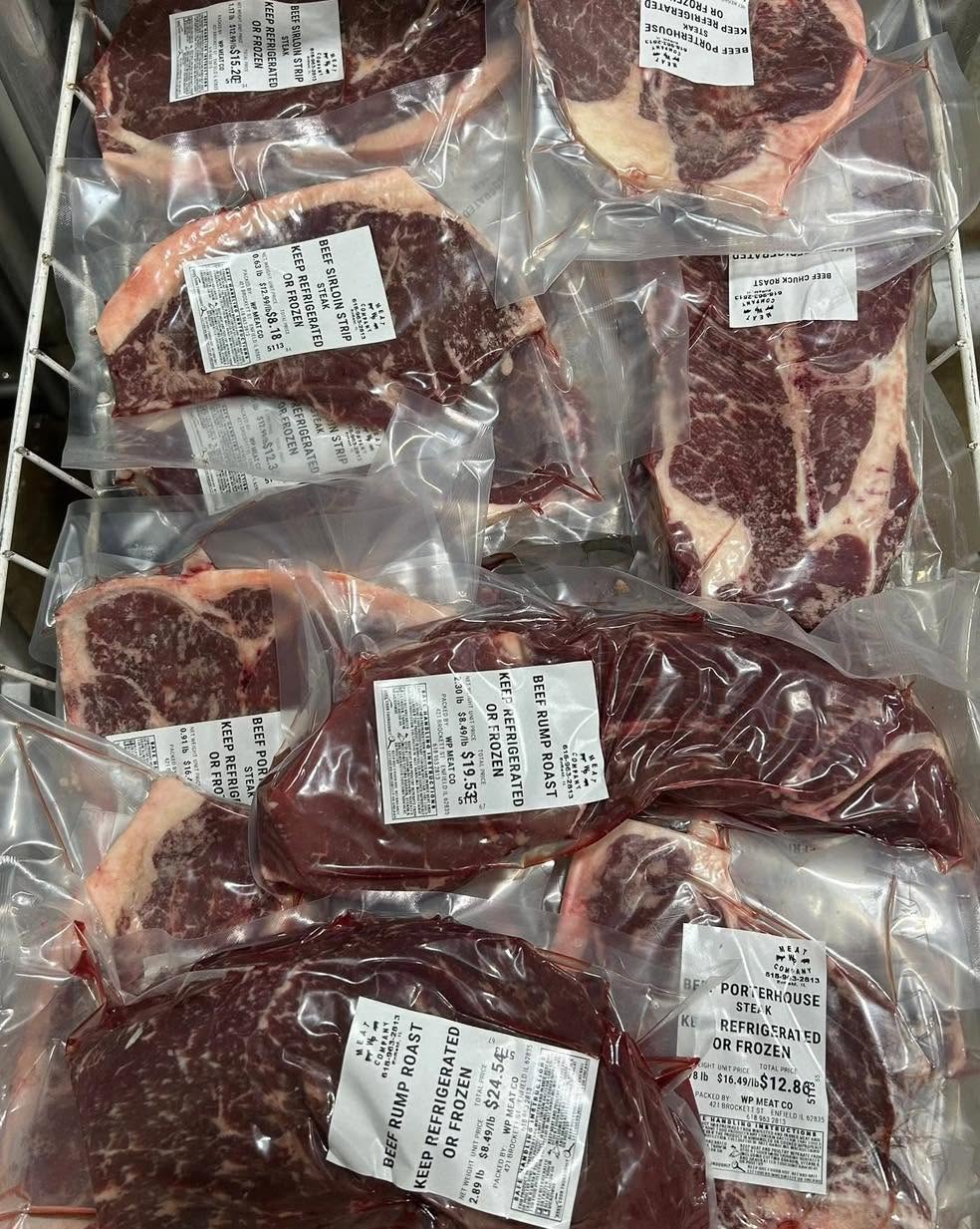 Multiple vacuum-sealed beef steaks and roasts in clear plastic bags with white product labels, arranged together in a storage offered at WP Meat Co in Enfield, Illinois.